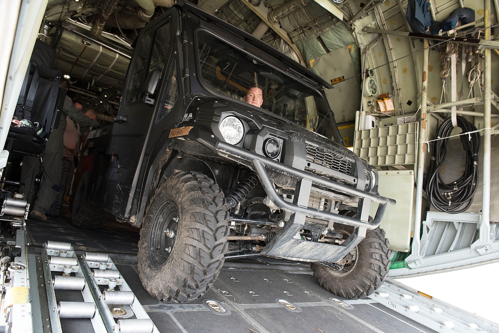 An all terrain vehicle is backed up the loading ramp into a C-130 cargo aircraft