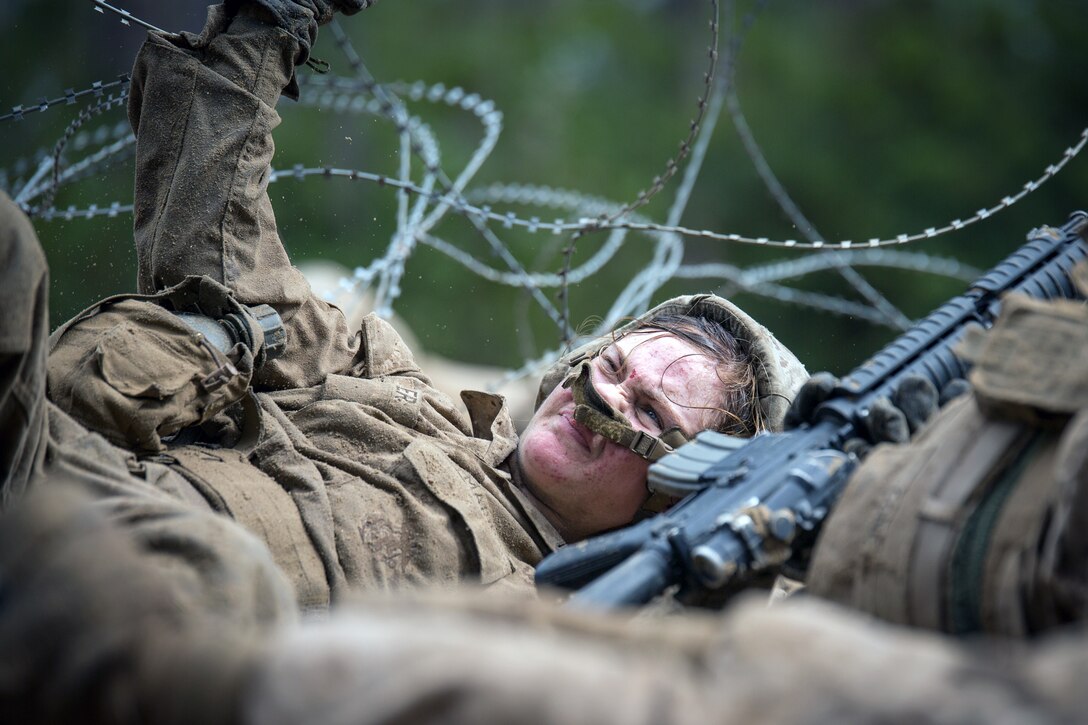 A Marine Corps recruit crawls under concertina wire.