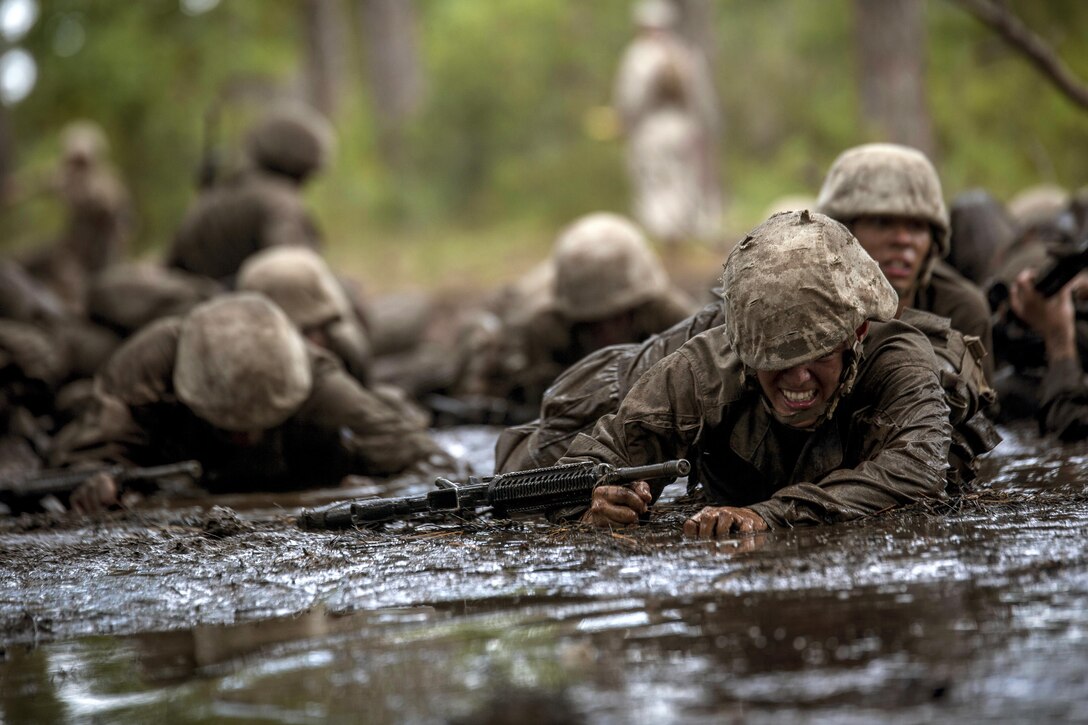 A recruit low-crawls through mud during the Crucible.
