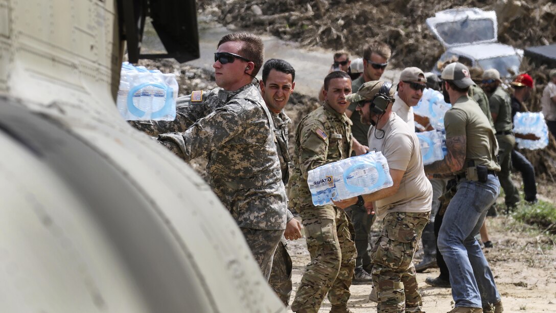 Soldiers and civilians in a line pass cases of water.