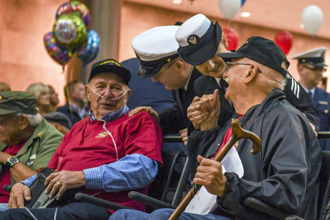 Sailors talk with veterans sitting in an airport seating area decorated with balloons.