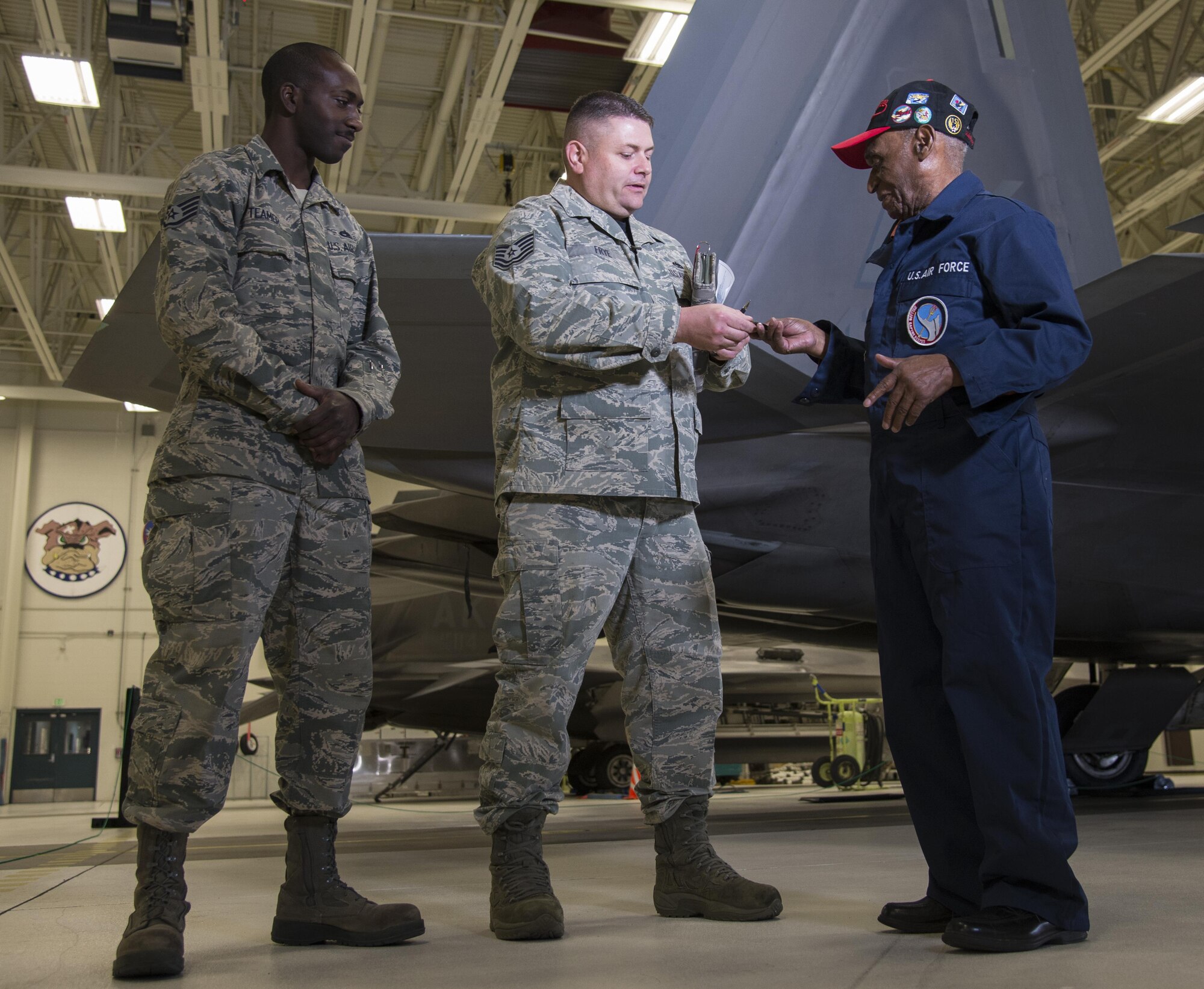 U.S. Air Force Tech. Sgt. Jeremiah Frye (middle), 477th Fighter Group quality assurance inspector, coins Army Air Corps Staff Sgt. Leslie Edwards, the last known living Tuskegee Airman of the 477th Bombardment Group, at Joint Base Elmendorf-Richardson, Alaska, Oct. 14, 2017. Edwards accompanied Frye for his 5,000th quality assurance inspection, a milestone he reached in nine years which typically takes 28 years to accomplish. In 2007, the 477th Bombardment Group became the 477th Fighter Group, bringing with it the legacy of Tuskegee Airmen to Alaska. (U.S. Air Force photo by Senior Airman Curt Beach)