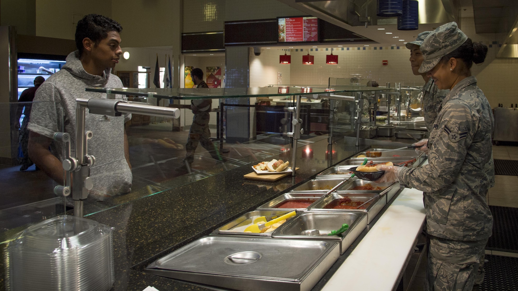 U.S. Air Force Airman 1st Class Antigone Falkner, right, and Airman 1st Class Randall Bagtas, both services apprentices assigned to the 6th Force Support Squadron, assists a customer in the dining facility at MacDill Air Force Base, Fla., Oct. 19, 2017. The MacDill dining facility serves approximately 800 to 1,000 customers daily. (U.S. Air Force photo by Senior Airman Mariette Adams)