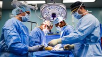 Medical personnel in blue surgical clothes perform surgery in an operating room.