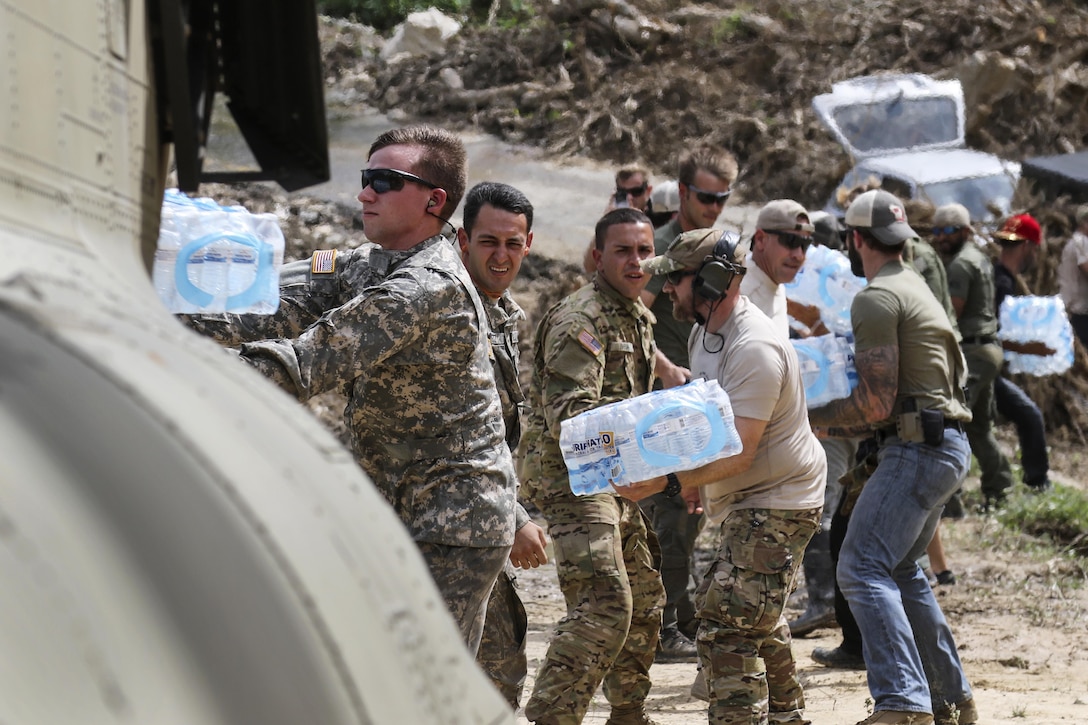 Soldiers and civilians in a line pass cases of water.