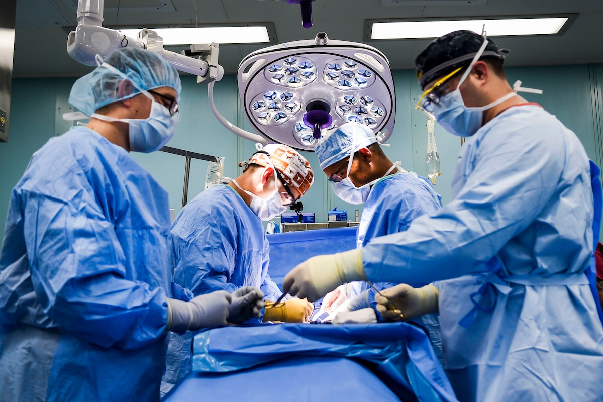 Medical personnel in blue surgical clothes perform surgery in an operating room.