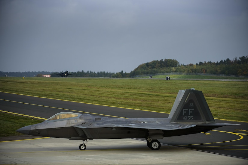 An F-22 Raptor assigned to the 1st Fighter Wing, Joint Base Langley-Eustis, Va., taxis while an F-16 Fighting Falcon assigned to the 480th Fighter Squadron lands at Spangdahlem Air Base, Germany, Oct. 13, 2017.