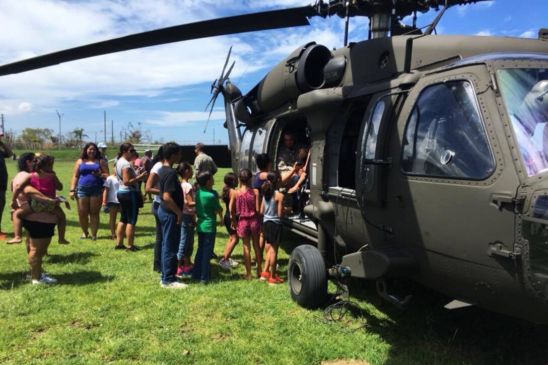 A line of people stand next to a helicopter.