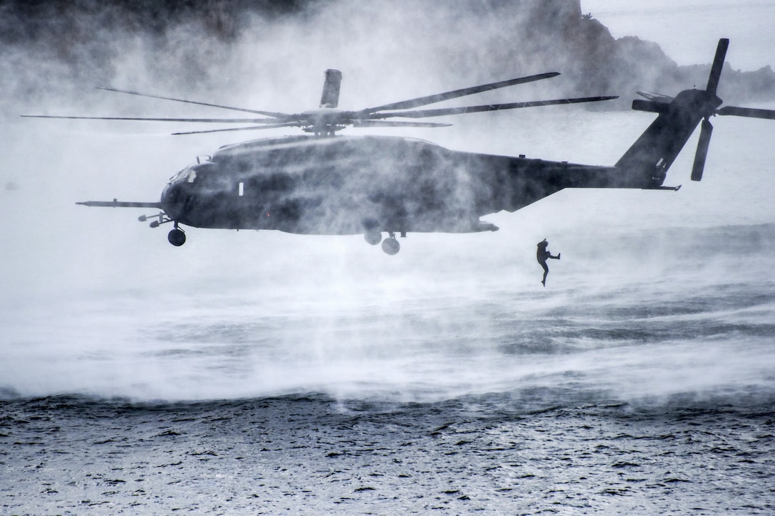 A diver jumps from a hovering helicopter into water.