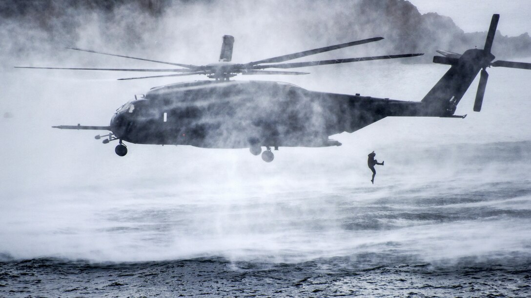 A diver jumps from a hovering helicopter into water.