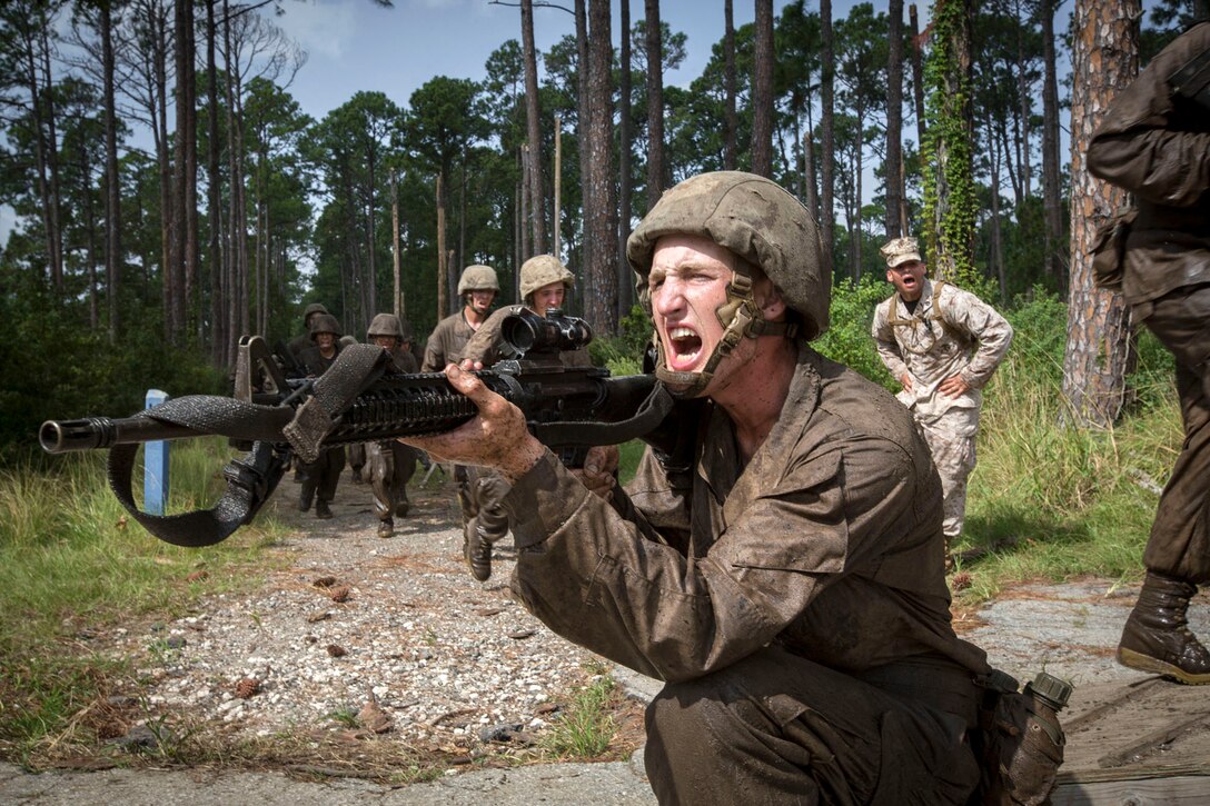 A Marine Corps recruit shouts while wielding a weapon in an outdoor training area.