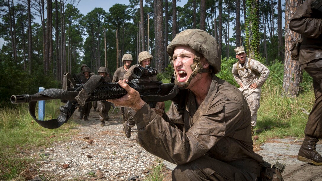 A Marine Corps recruit shouts while wielding a weapon in an outdoor training area.