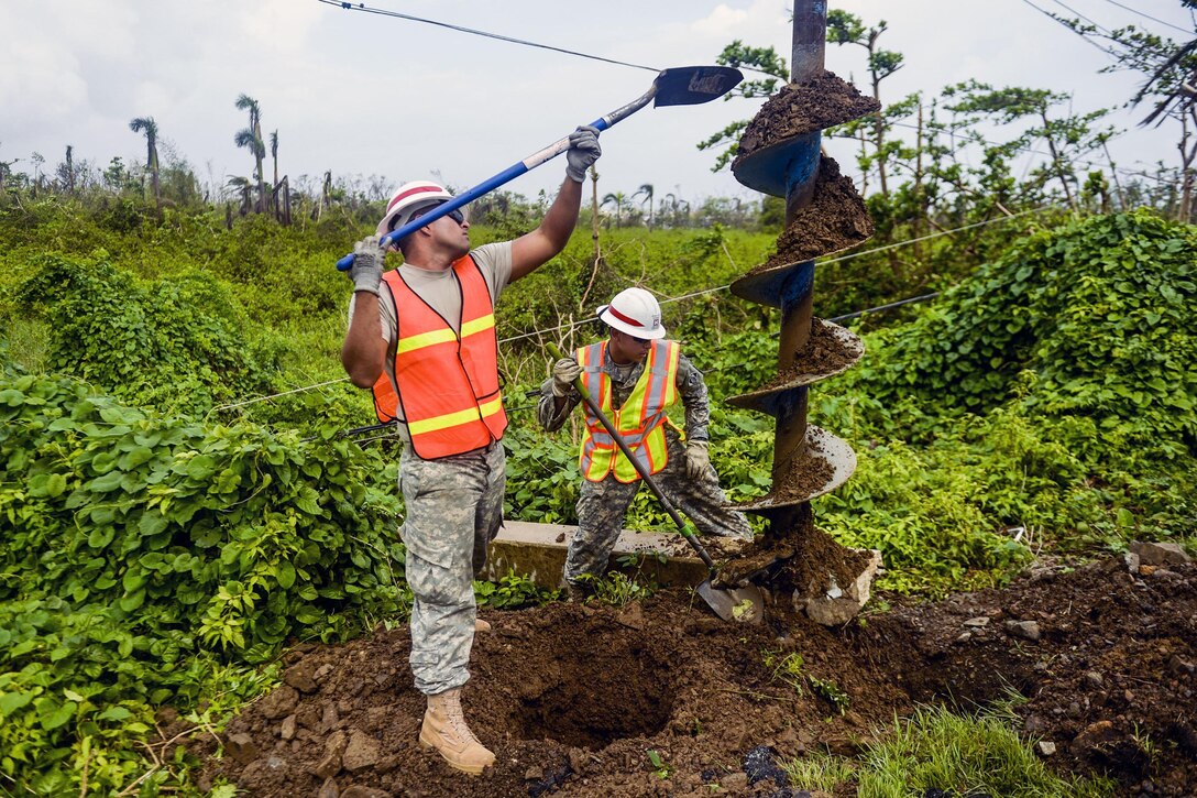 Two soldiers with shovels work with an auger