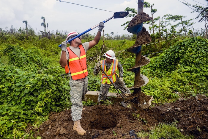 Two soldiers with shovels work with an auger.