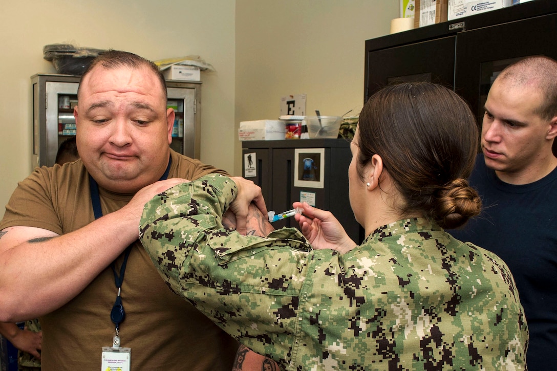 A sailor gives a shot to another sailor, as a third observes.