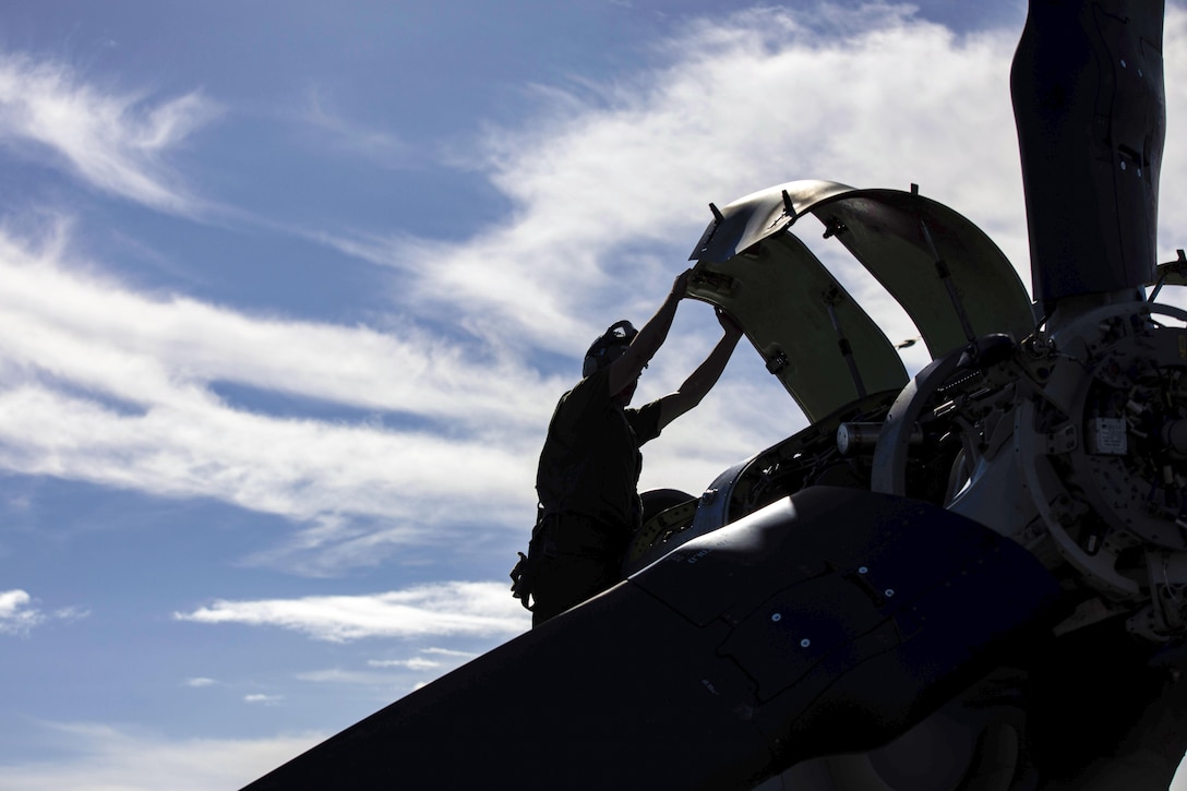 A Marine, shown in silhouette, reaches up and holds part of an aircraft's external structure.