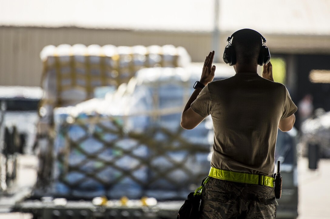 An airman signals with his arms toward a loader carrying pallets of water.