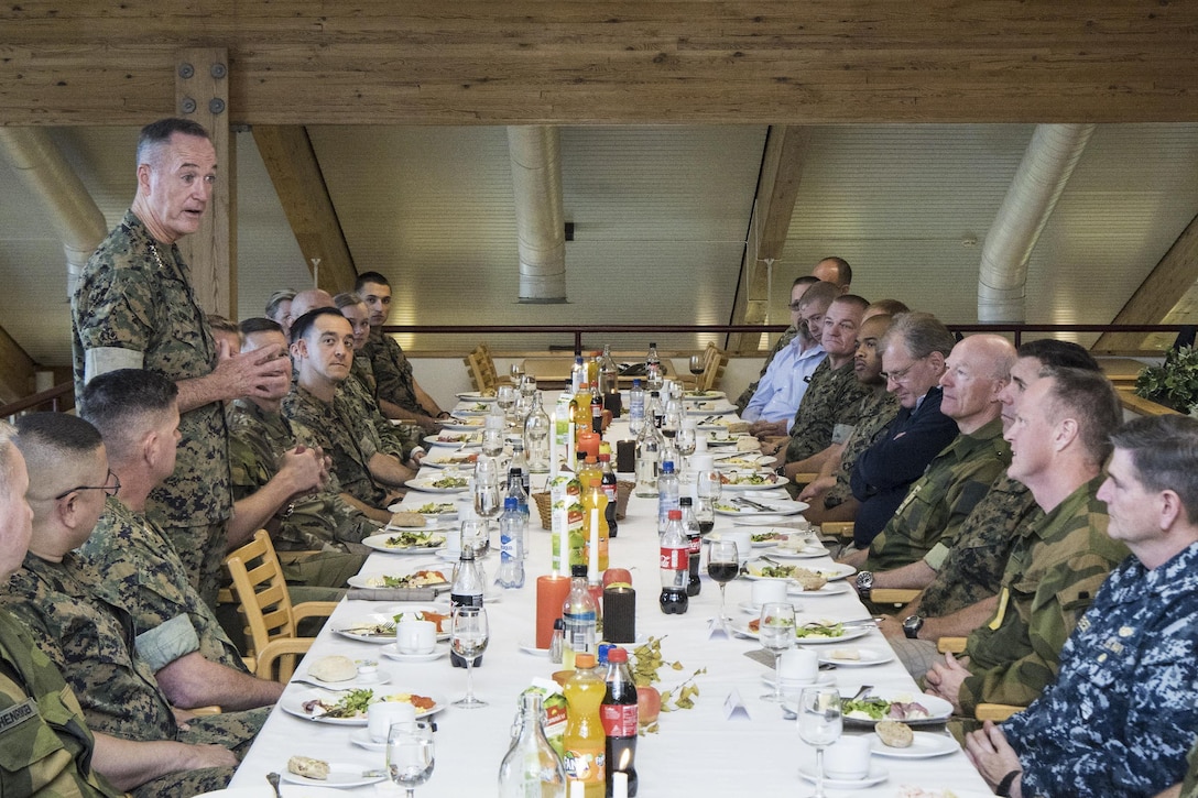 The chairman of the Joint Chiefs talks to troops at a long table.