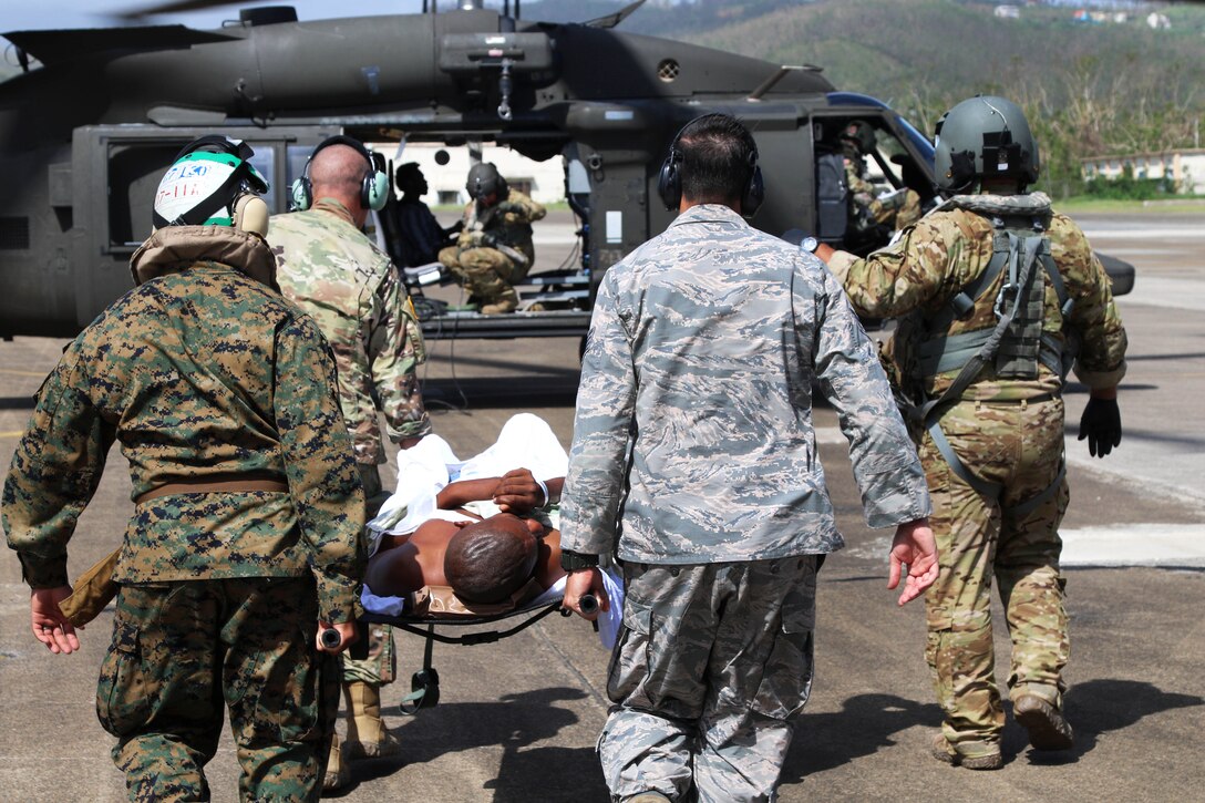 Service members carry a person toward an aircraft.