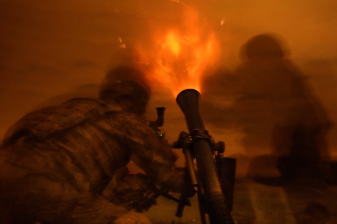 Soldiers fire a mortar system at night.