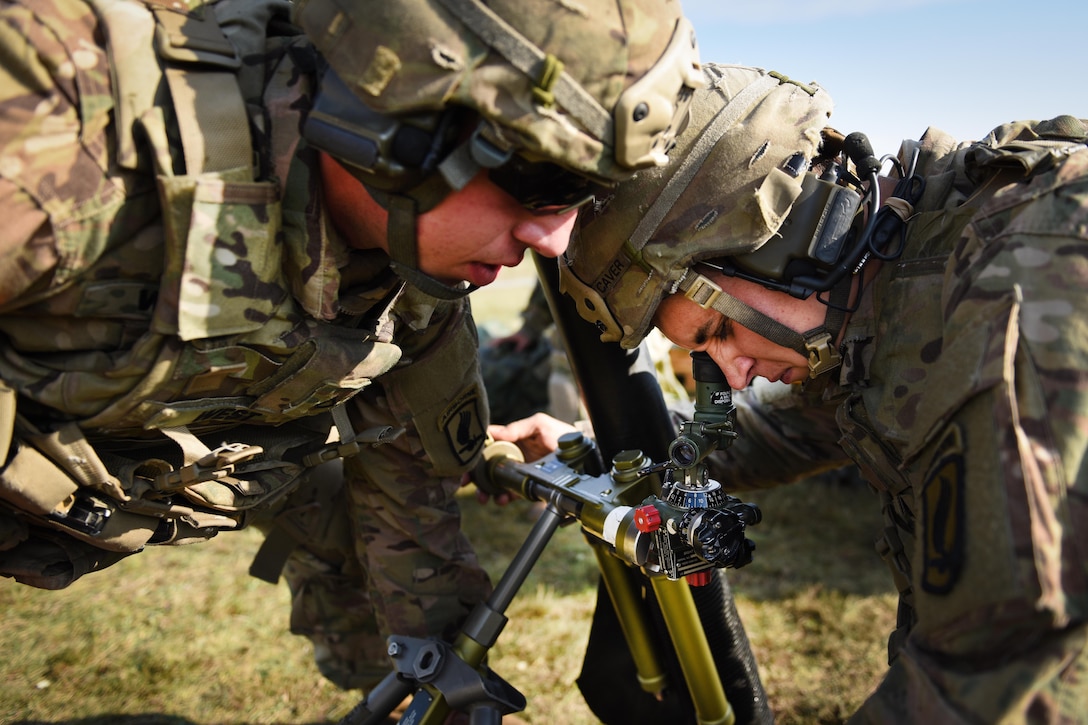 Two soldiers lean over a mortar system sight.