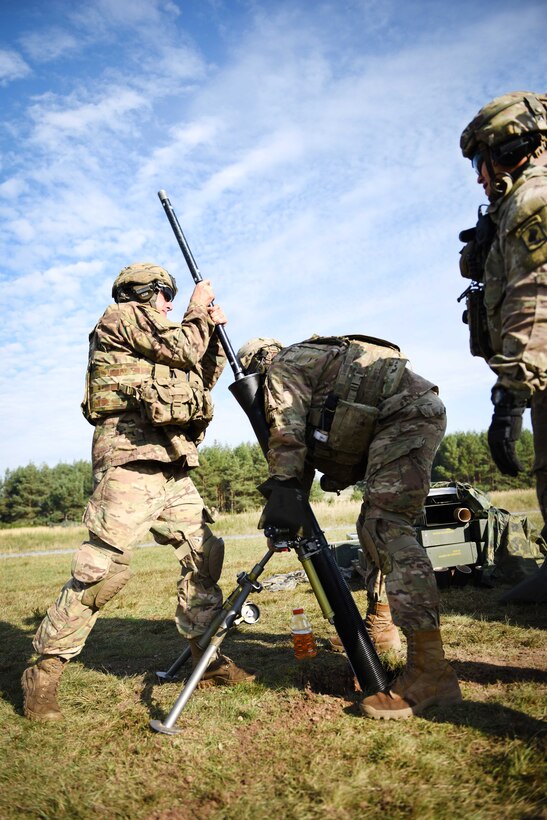 Three soldiers clean a mortar system on a range.