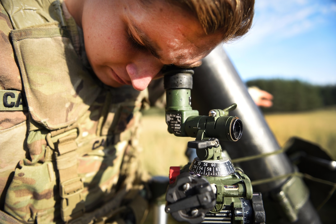 A soldier looks into a sight on a mortar system.