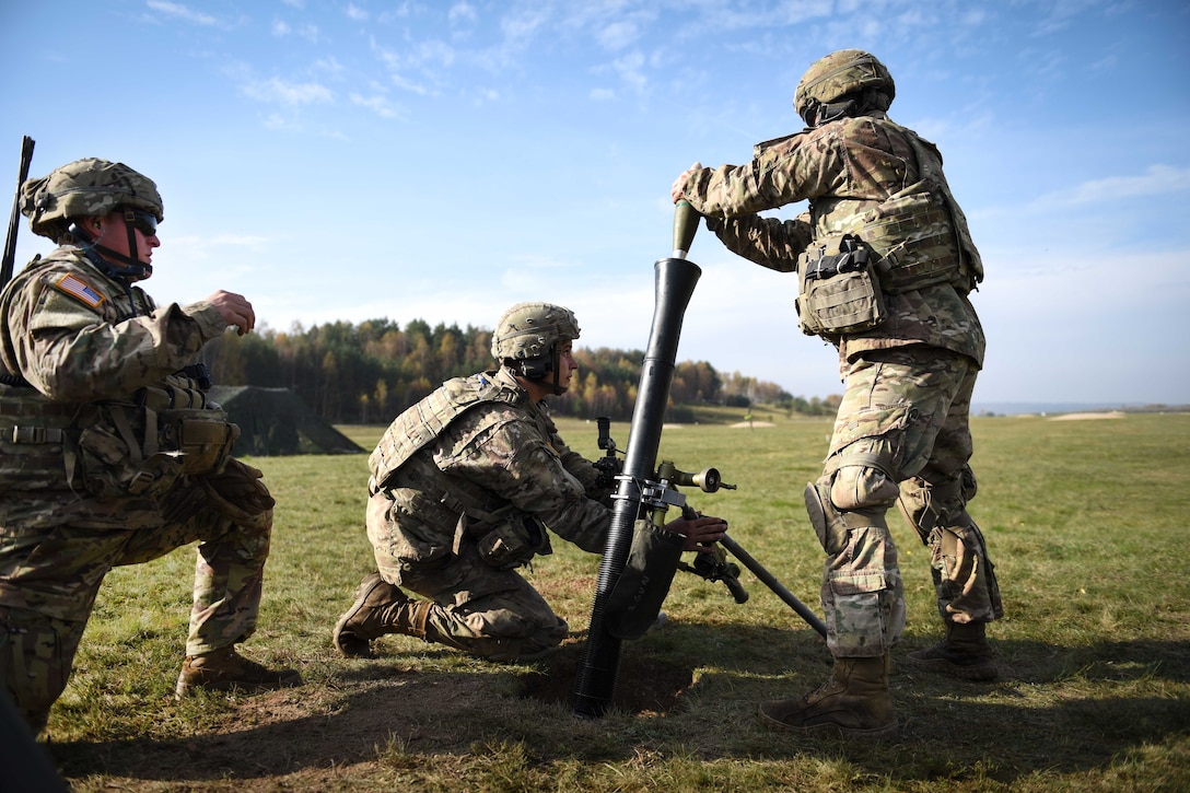 Three soldiers load a mortar system.