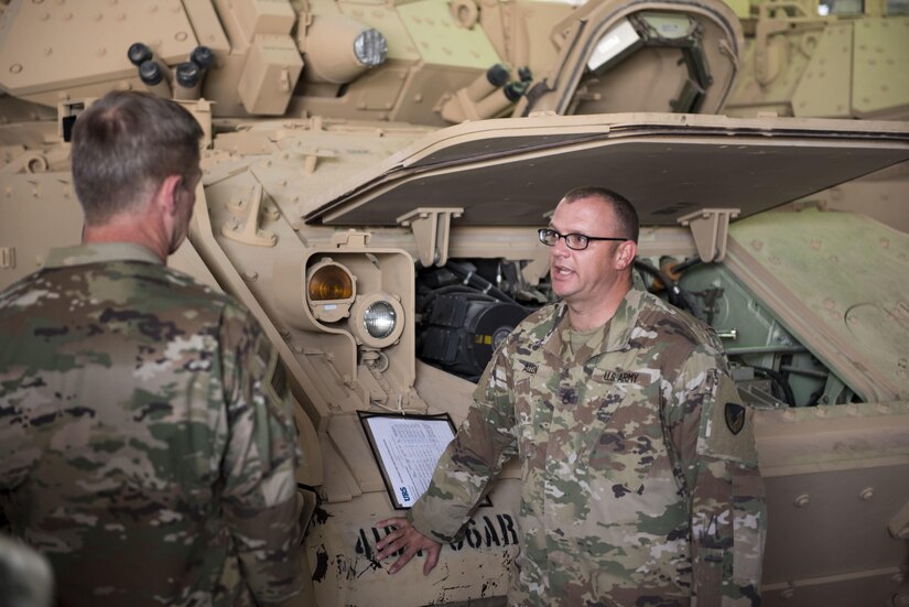 Two soldiers speaking in front of an Army vehicle