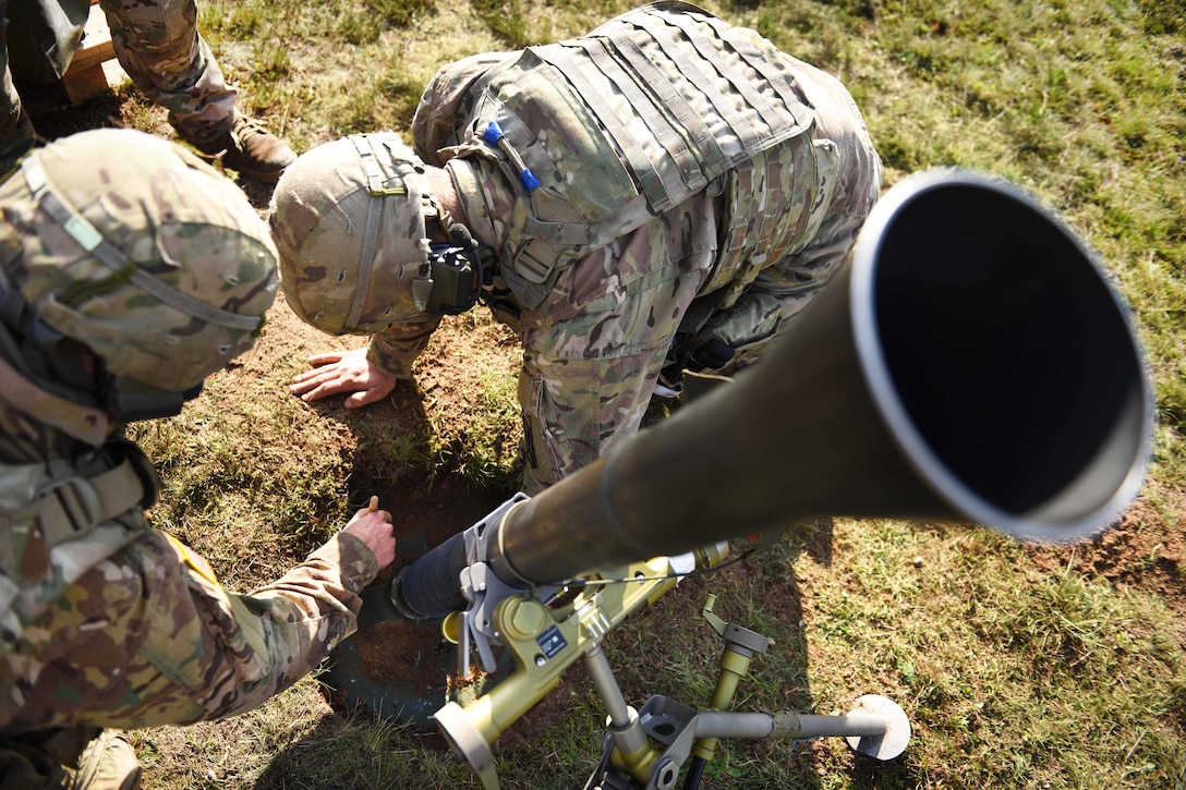 Two soldiers lean over a mortar system to clean it.