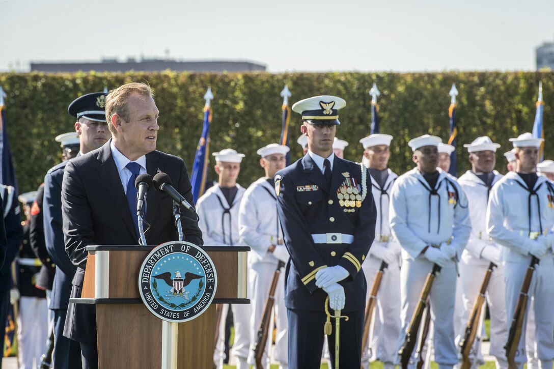 The deputy defense secretary speaks during a ceremony with sailors behind him.
