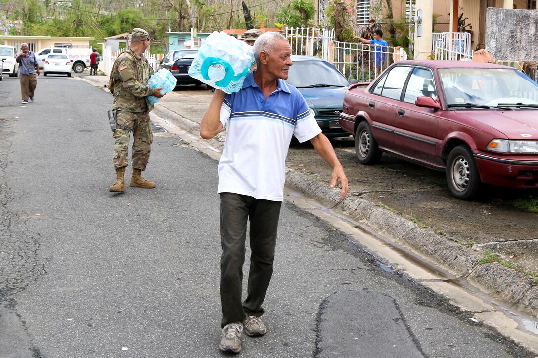 A resident carries a case of water to his home in Puerto Rico.