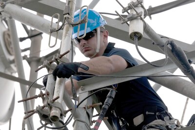 An airman works on wires up in a tower.