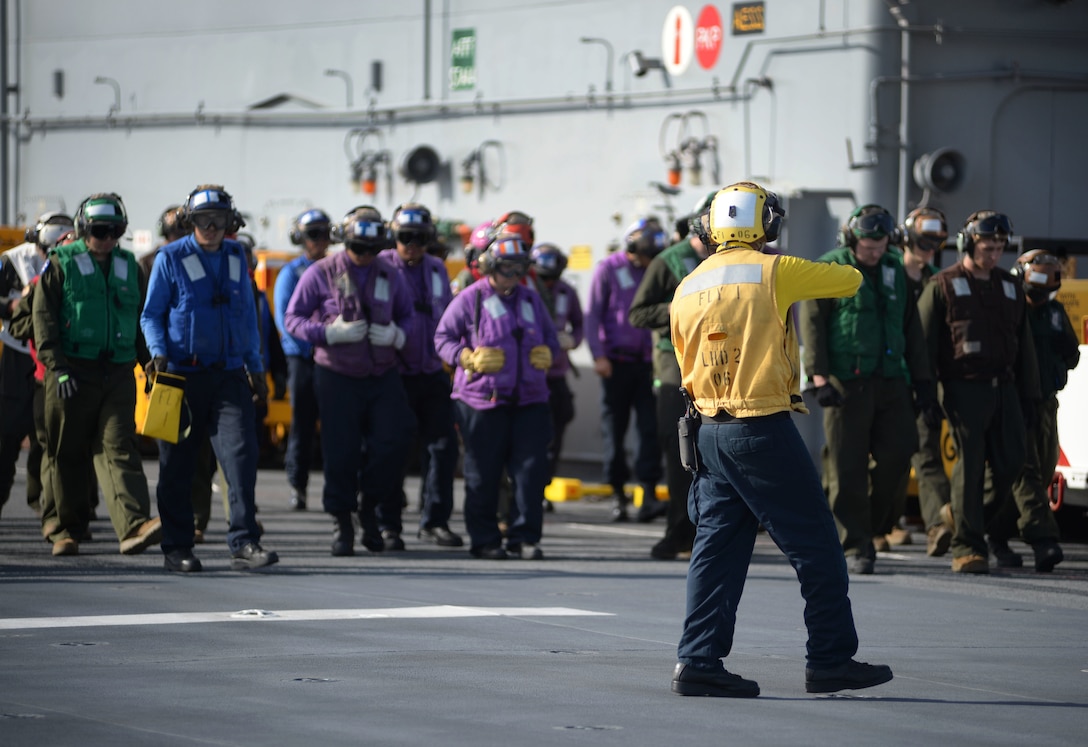 Navy Petty Officer 3rd Class Chinedu Darlington directs sailors and Marines during a combat foreign object debris search on the flight deck of the amphibious assault ship USS Essex.