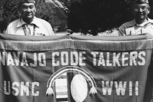 Two people hold up a banner that reads: Navajo Code Talkers USMC WWII