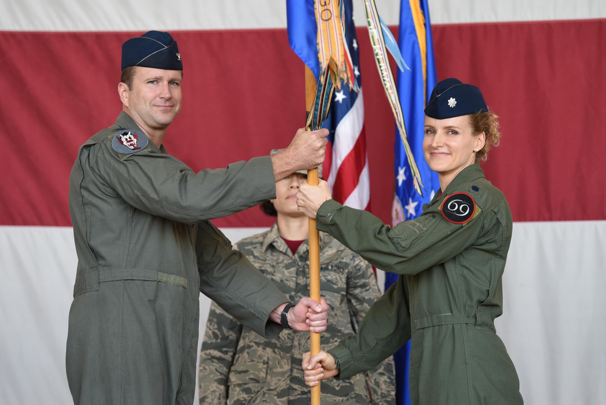 Col. Korey Amundson, 944th Operations Group commander passes the guidon to Lt. Col. Trena Savageau, incoming 69th Fighter Squadron commander during a change of command ceremony Oct. 10.