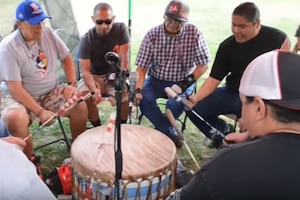 A group of people in a circle bang a drum.