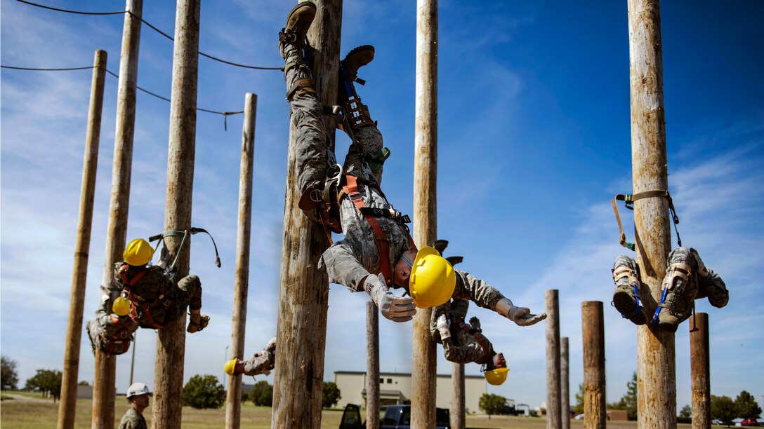 Airmen use their legs to hang from multiple tall wooden poles.