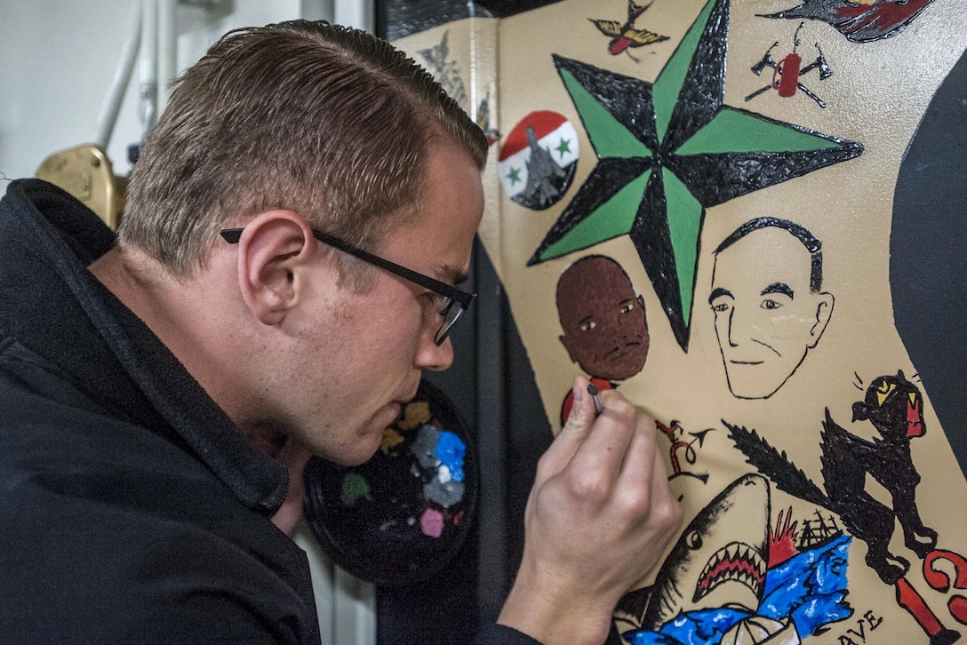 A sailor paints a design on a workshop door on a ship.