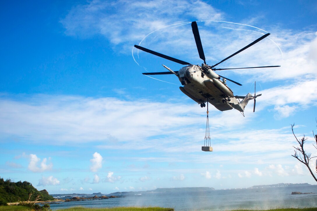 A CH-53E Super Stallion helicopter hovers over a landing zone with a cement block during an external lift drill.