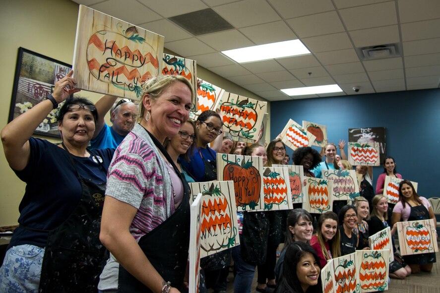Participants pose with their finished paintings during a Painting with a Twist event, Oct. 21, 2017, at Moody Air Force Base, Ga. At the event, participants went through the steps to paint a festive fall pumpkin. The event was geared toward providing fun painting experiences for Active Duty members and their dependents, which can help ease some of the stress they face as military families. During the event, participants went through the steps to paint a festive fall pumpkin.  (U.S. Air Force photo by Airman 1st Class Erick Requadt)
