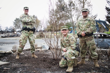 California Guard Soldiers nurture a tree amid fire ruins