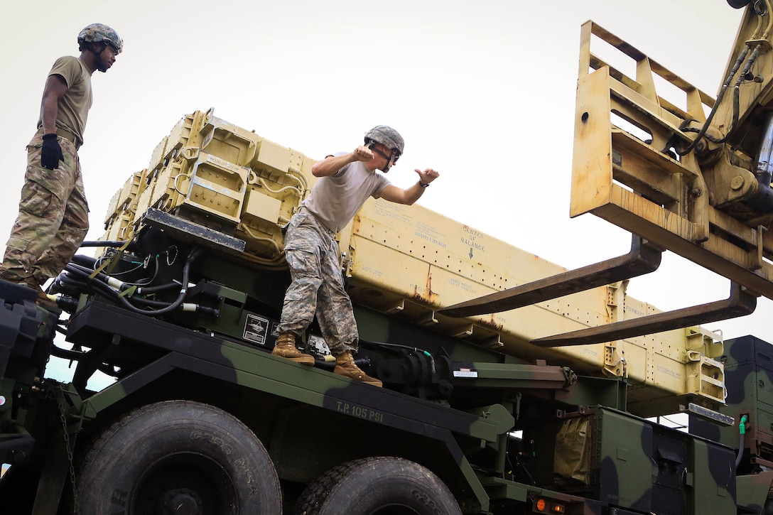 A soldier guides a forklift offloading a Patriot missile system equipment.