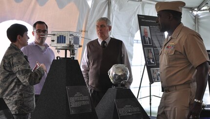 IMAGE: DAHLGREN, Va. (Oct. 16, 2017) – Maj. Erin Dunagan, U.S. Air Force 18th Space Control Squadron, Detachment One commanding officer, briefs civilians and Capt. Godfrey ‘Gus’ Weekes, Naval Surface Warfare Center Dahlgren Division commanding officer about two satellites on display at the exhibit tent during the centennial kickoff celebration of the Navy base at Dahlgren. The satellite, pictured left, was launched on Aug. 13, 1965 when the space surveillance system was converted to a new operating frequency and it served as a signal source (mHz) for determining if all the surveillance system antenna elements were correctly adjusted in phase. The circular nine-inch diameter satellite was launched on March 9, 1965 as a target for the Navy’s space surveillance system. The unusual design of this small satellite permitted it to become a large space target 50 feet in diameter. The Navy transferred operation of the former Naval Space Surveillance System – the nation's oldest sensor built to track satellites and debris in orbit around the Earth – to the Air Force on Oct. 1, 2004. The 18th Space Control Squadron maintains continuous and transparent space situational awareness to assure global freedom of action in space.