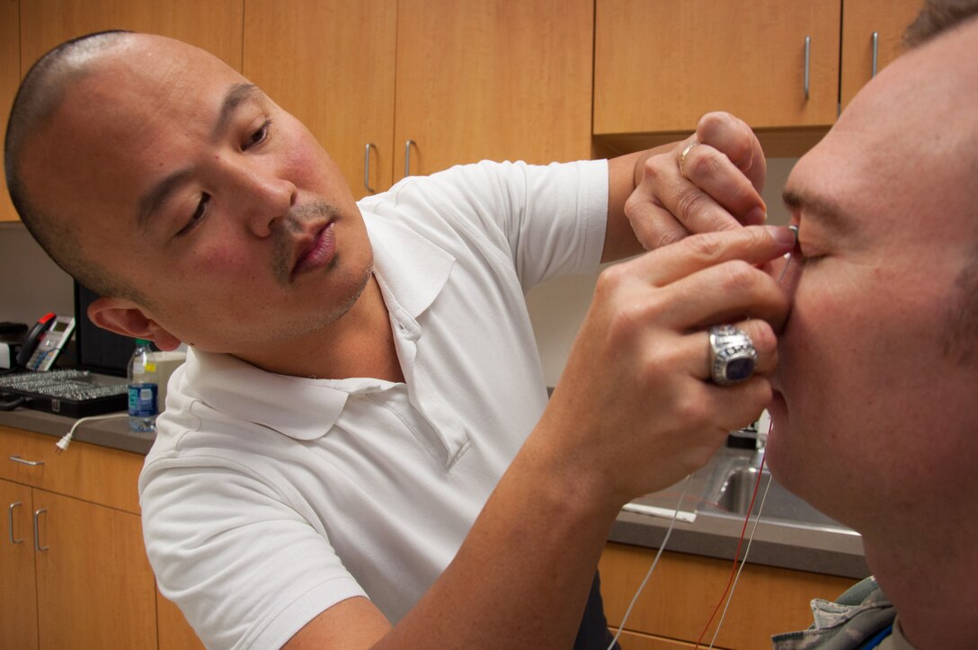 Dino Tsuchiyama (left), Aeromedical Consultation Service Ophthalmology Branch electro-diagnostic technician, attaches electrodes to Lt. Col. Christopher Cannon in order to measure how well the retinas in Cannon’s eyes react to light. Ophthalmological electrophysiology studies the electrical activity of the eyes. (U.S. Air Force photo/John Harrington)