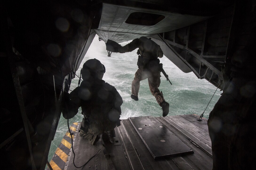 A service members jumps from the back of a helicopter.