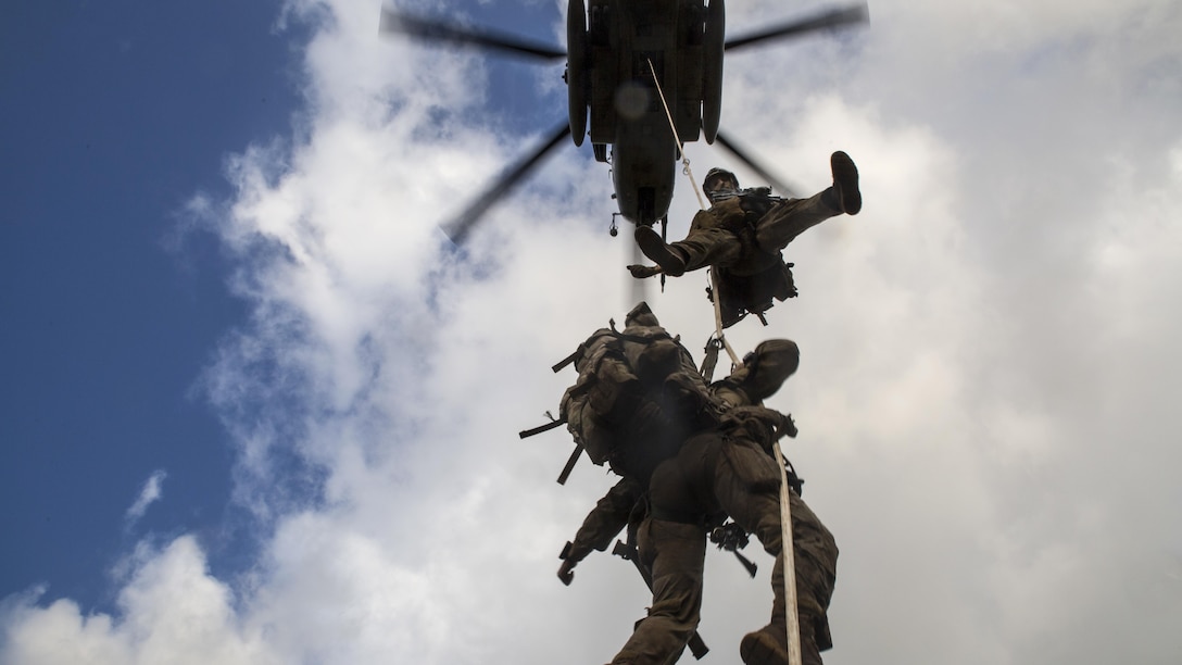 Troops dangle off a rope from a helicopter overhead during a course.