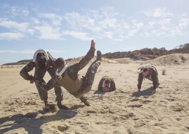 A Marine participating in U.S. Marine Corps Forces command’s Marine Corps Martial Arts Program Instructor Course executes a shoulder throw while his teammates do push-ups at Fort Story in Virginia Beach, Va., Oct. 19. Marines were required to demonstrate all techniques in their MCMAP level and below before they were awarded the tan instructor tab at the end of the course. (Official Marine Corps photo by Chris Jones/Released)