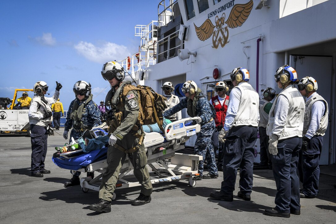 Sailors escort a patient on a ship for transport to a hospital.