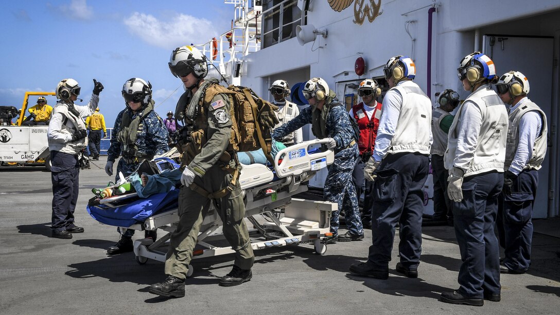 Sailors escort a patient on a ship for transport to a hospital.